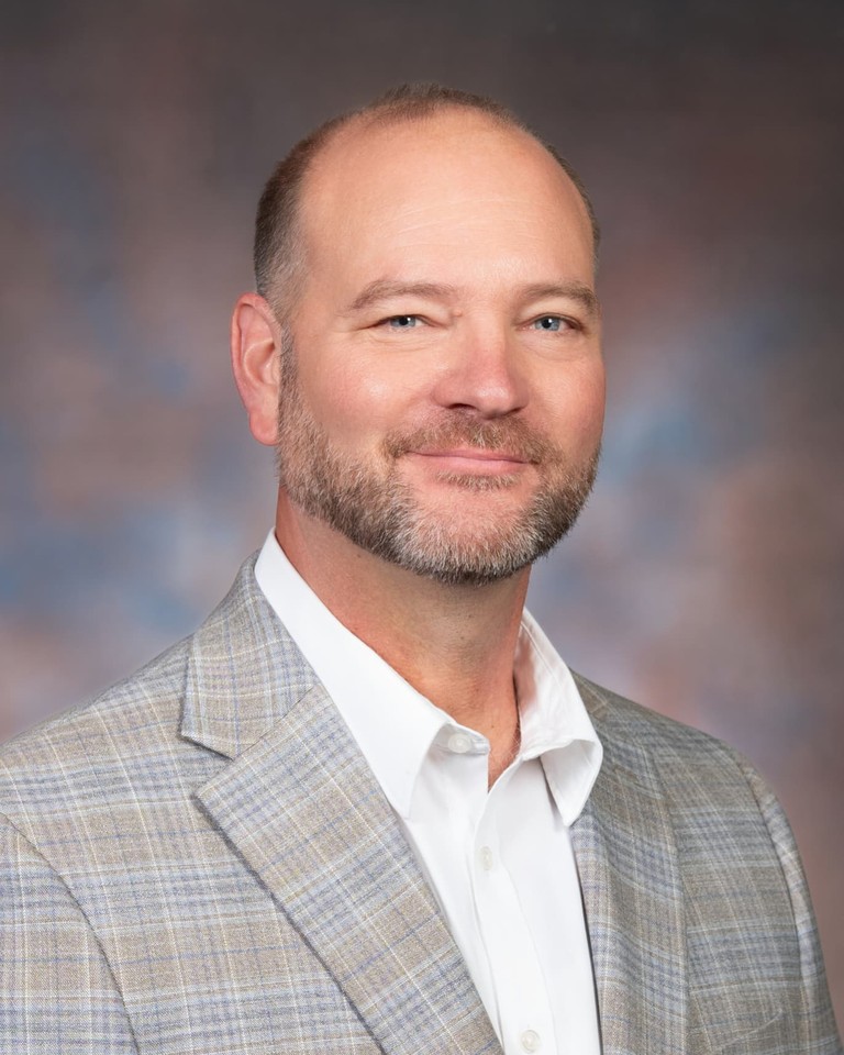 Portrait of Rob Mann smiling in a light plaid blazer and open-collar white shirt